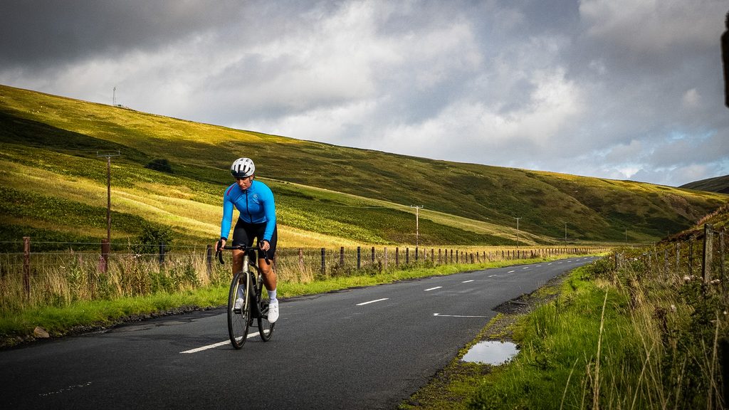 Fietser in een blauw shirt klimt over een weg langs kale heuvels in de Scottish Borders