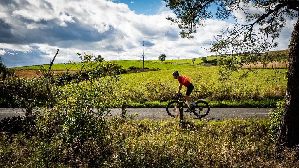 Fietser op een landweg tussen groene akkers en bomen in de Scottish Borders