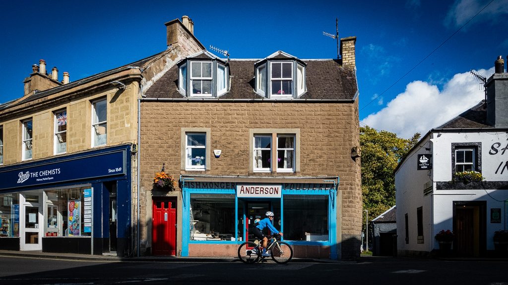 Fietser rijdt langs een winkel met blauwe pui in een Schots marktstadje