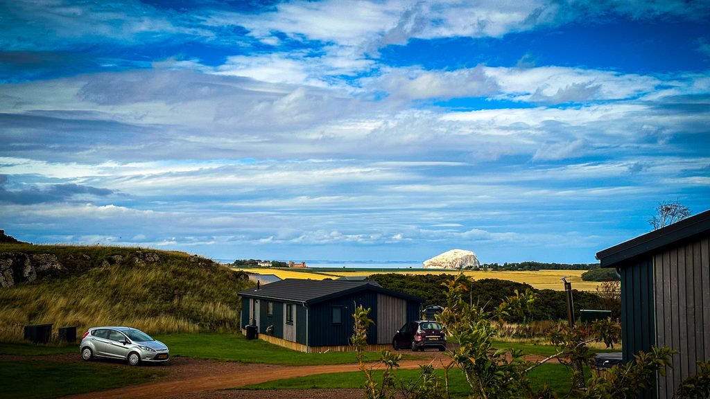 Donkere houten lodges van Landal Whitekirk Hill op een grasveld, met Bass Rock wit aan de horizon