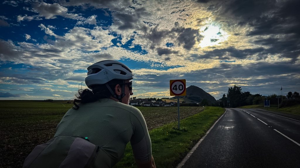 Fietser naast een 40-bord op een landweg, met de heuvel North Berwick Law tegen een zonnige wolkenlucht