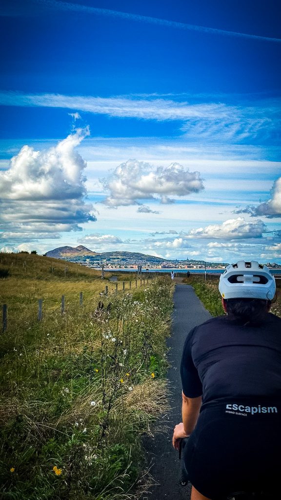 Fietser op een smal pad door het gras, met Edinburgh in de verte