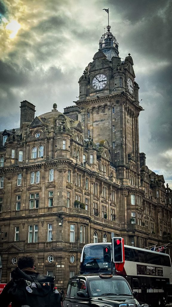 Klokkentoren van het Balmoral Hotel in Edinburgh onder een dreigende wolkenlucht, met een rode dubbeldekker