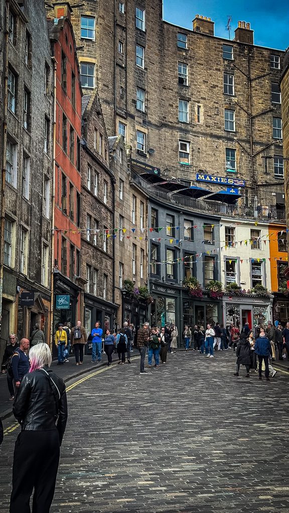 Kleurrijke winkelgevels en kasseien in de bochtige Victoria Street in Edinburgh, vol wandelaars