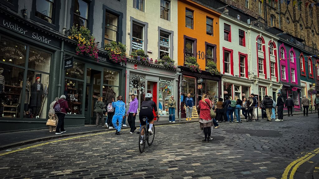 Fietsers en wandelaars op de kasseien tussen kleurrijke winkelpuien in het centrum van Edinburgh
