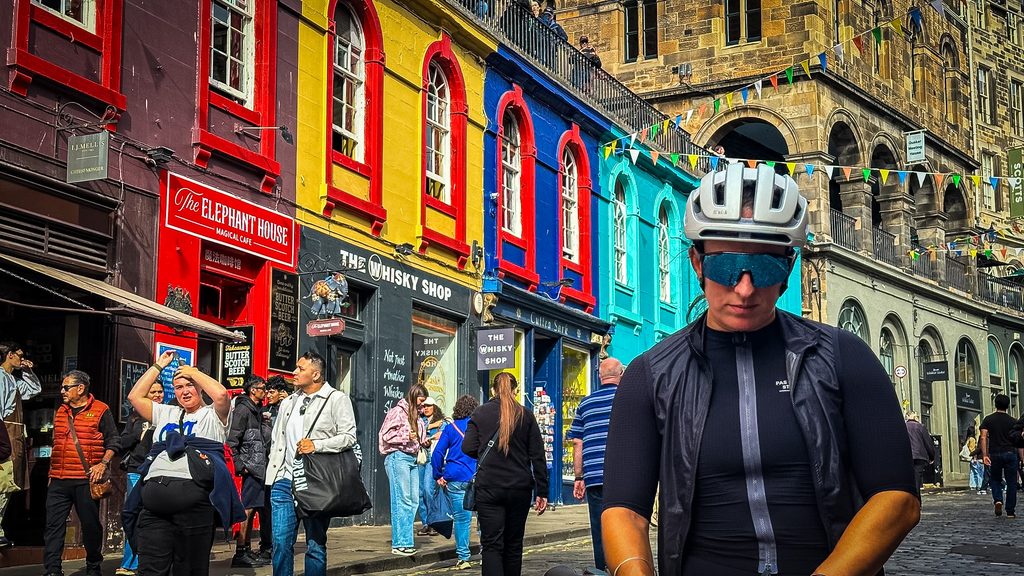 Fietser met helm en zonnebril voor de kleurrijke gevels van West Bow in Edinburgh