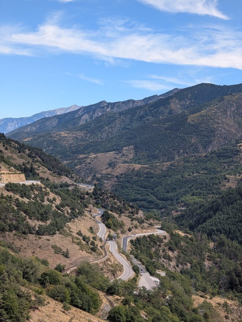 Uitzicht op een kronkelende weg diep in een bergdal onder een blauwe lucht