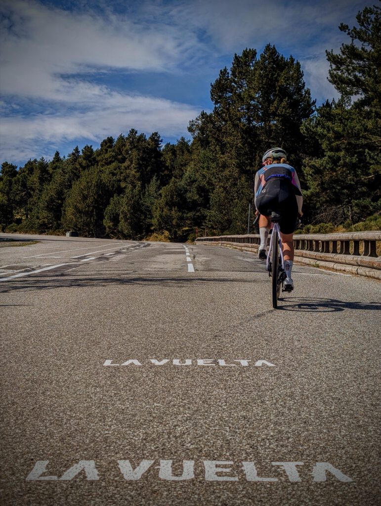 Cyclist rides over a road on which La Vuelta is painted in large white letters